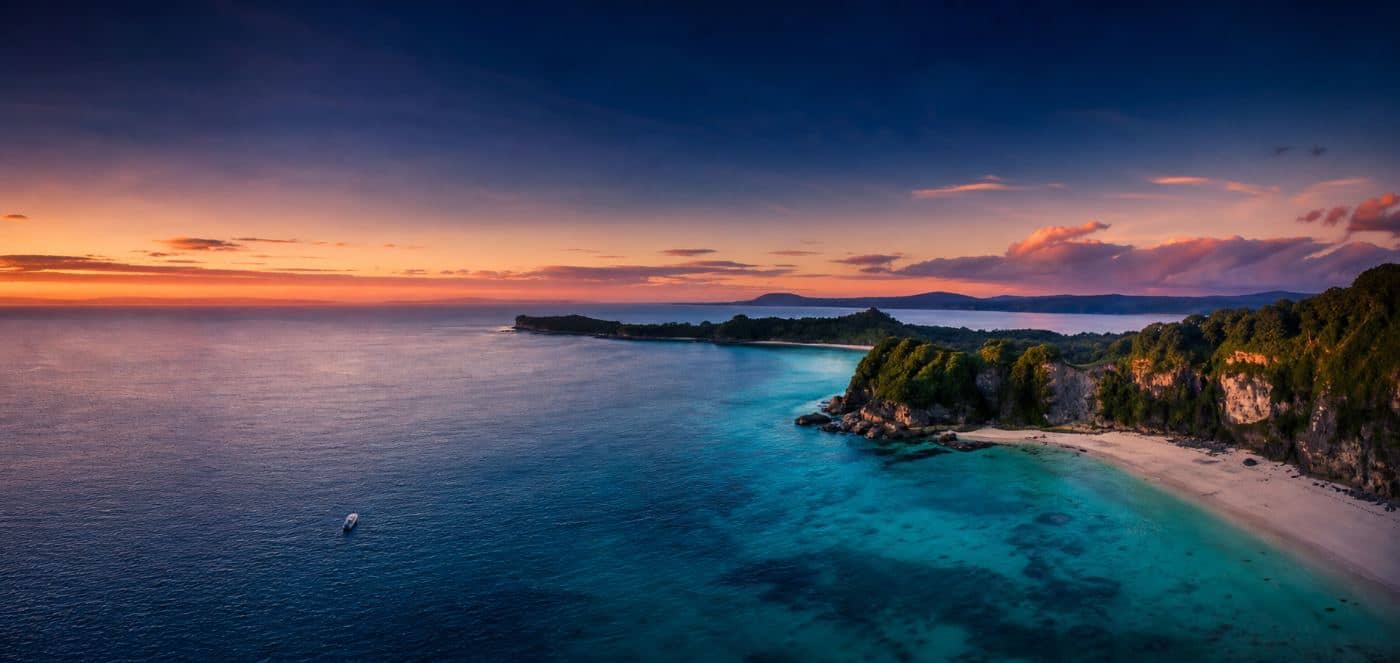 Aerial view of a sunlit coastline with turquoise water meeting a curved sandy bay